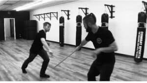 Two men practicing stick defense in a martial arts gym.