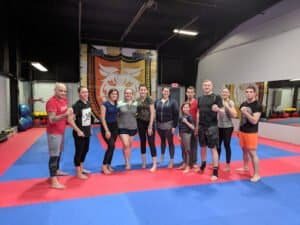 People standing in a martial arts training facility with mats and a lion logo.
