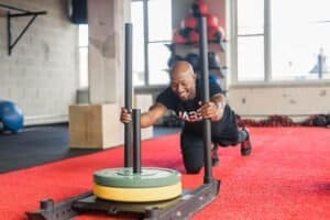 Male boxer pushing weighted sled for strength training at gym.