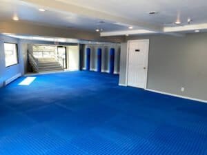 Spacious kickboxing training room with blue mats and punching bags.