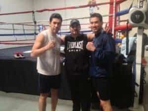 Two boxers and coach posing in boxing gym with gloves and ring.