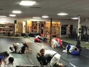 MMA fighters practicing grappling techniques on mats in gym.