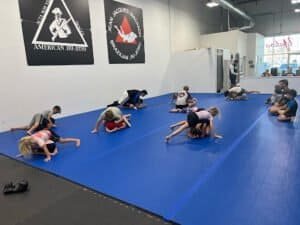 Children practicing Brazilian Jiu-Jitsu on blue mats in a martial arts gym.