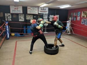 Young boxers practicing sparring in a boxing gym with punching bags and training equipment.